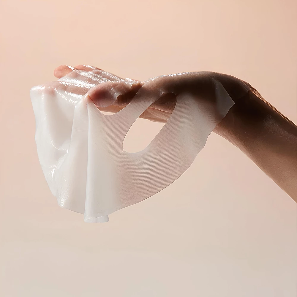 Hand holding a white, soft, and fluffy face mask against a beige background