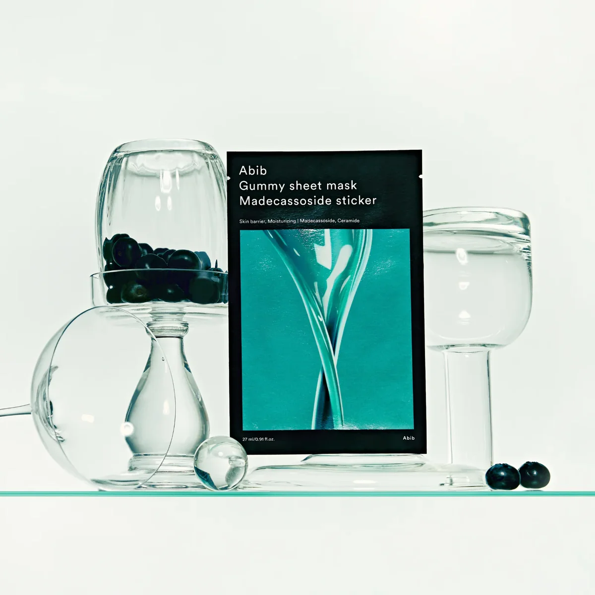 Sheet mask packaging with glass containers and berries on a white background